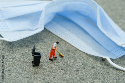 Miniature people toy figure photography. A sweeper cleaning worker sweeping used blue latex glove on the floor