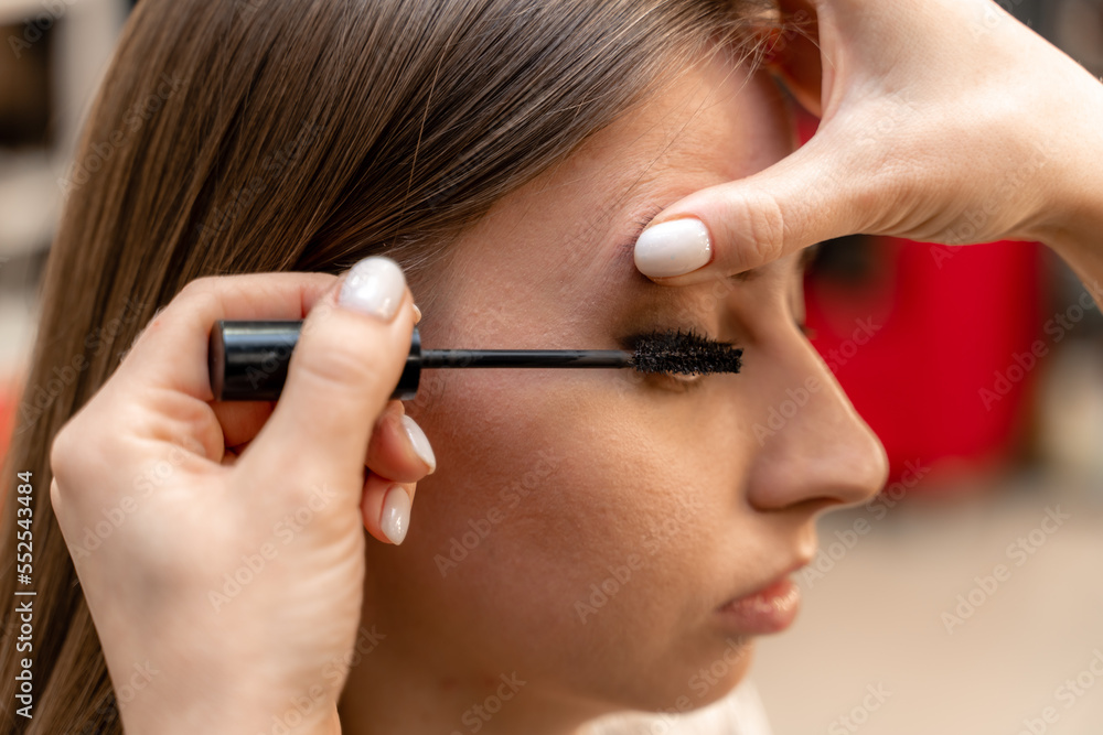 Makeup artist paints eyelashes to a woman in a beauty salon.