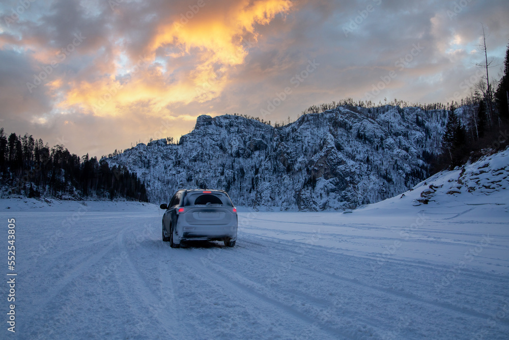 Winter travel. The car against the backdrop of a winter landscape, white snow, sunset sky, mountains in the background.