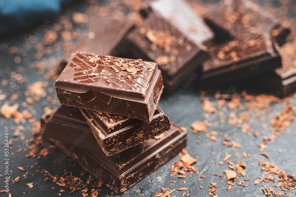 Dark chocolate bar pieces on dark background with grated chocolate and spices, pile chunks of broken chocolate Dark chocolate bar pieces on dark background with grated chocolate and spices, pile chunks of broken chocolate