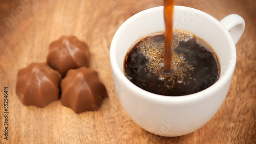 Pouring black coffee in white cup. Coffee with chocolate candy