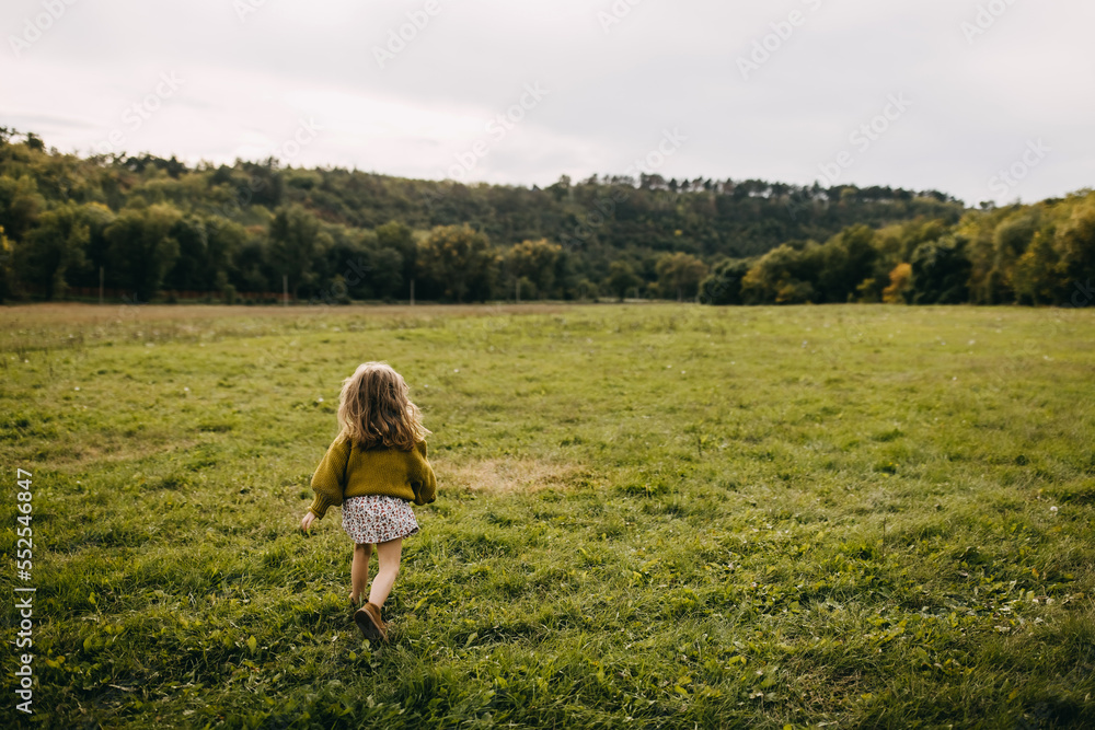Little girl running in an open field with green grass, wearing a dress and a sweater. Little girl running in an open field with green grass, wearing a dress and a sweater.