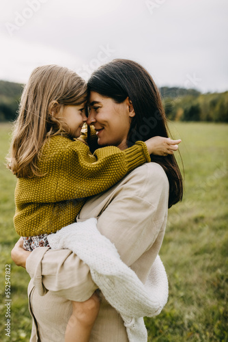 Closeup portrait of pregnant woman and her toddler daughter playing nose to nose. Mother hugging little girl, holding in arms, touching noses.
