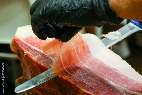 knife slicing a slice of raw ham and the  glove photo