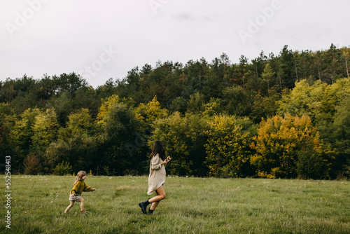 Pregnant woman and her toddler daughter outdoors, running in a field with green grass, spending time together.