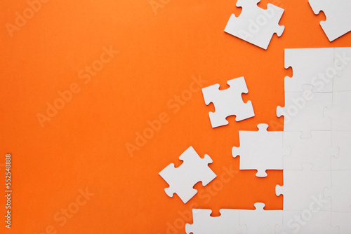 Unfinished white jigsaw puzzle pieces on orange background
