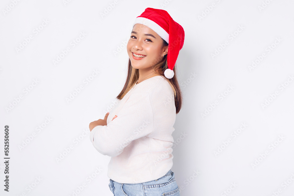 Smiling young Asian woman in Santa Claus hat with crossed arms looking at camera over white background Smiling young Asian woman in Santa Claus hat with crossed arms looking at camera over white background