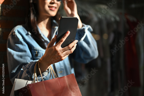 Fashionable woman carrying shopping bags and using smart phone at outdoor on sunny day