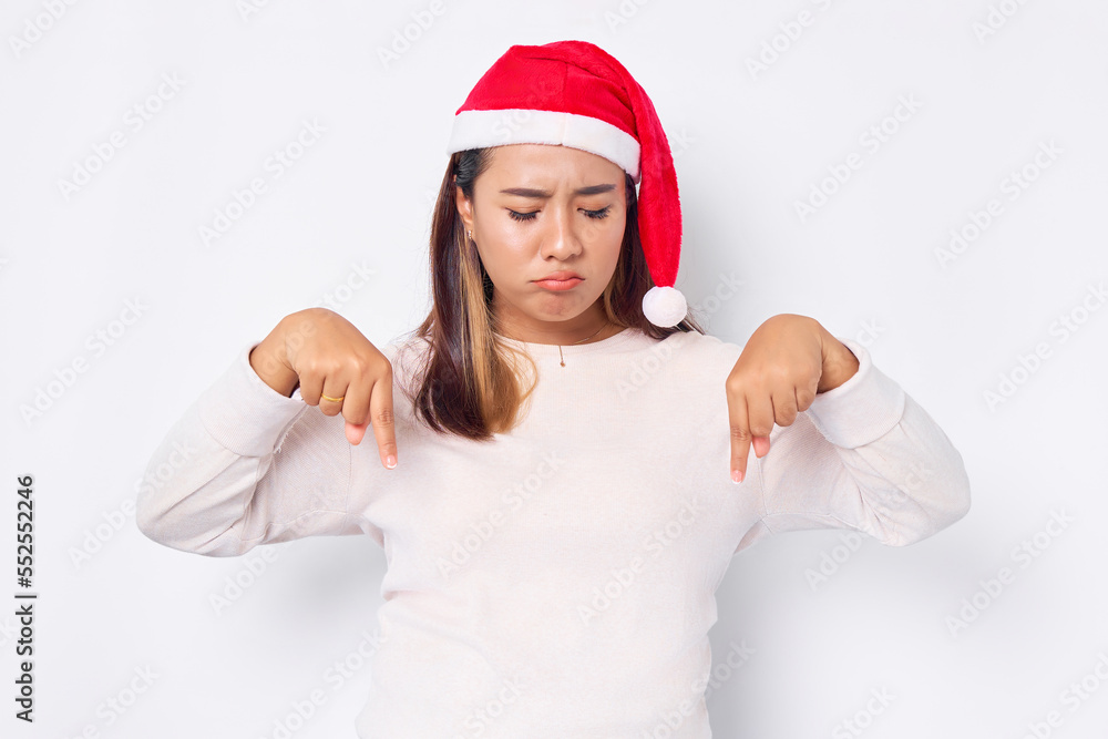 Pensive young Asian woman in a Christmas hat pointing fingers down, inviting people to follow isolated over white background. celebration Christmas holiday and New Year concept Pensive young Asian woman in a Christmas hat pointing fingers down, inviting people to follow isolated over white background. celebration Christmas holiday and New Year concept