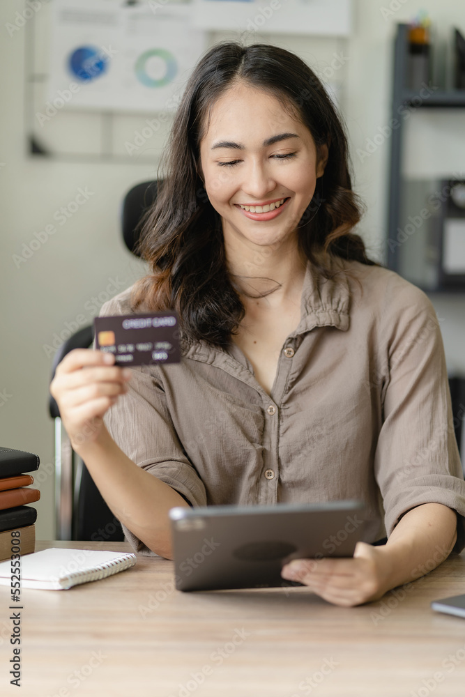 Happy young asian woman shopping online at home She holds a credit card and uses a tablet. online banking payment communication network internet wireless application Happy young asian woman shopping online at home She holds a credit card and uses a tablet. online banking payment communication network internet wireless application