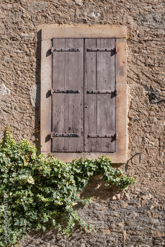 Window covered in closed, rustic wood shutters set in an old stone wall with ivy on a home in a French village photo