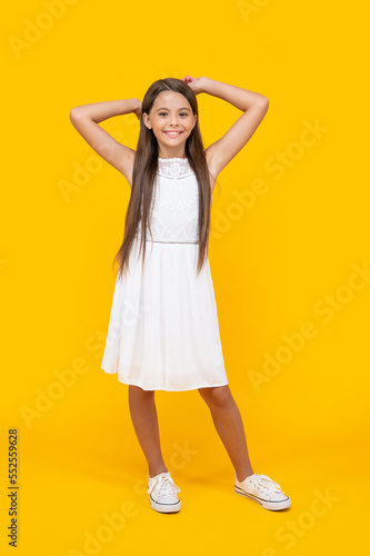 cheerful teen child in white dress standing on yellow background