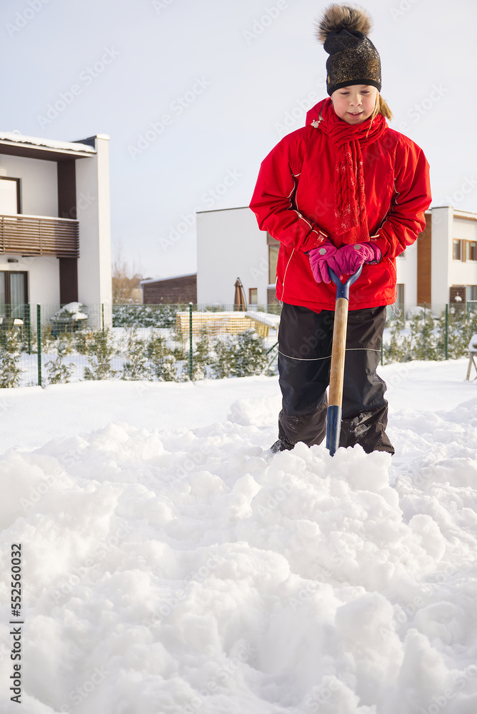 Girl shoveling snow on home drive way. Beautiful snowy garden or front