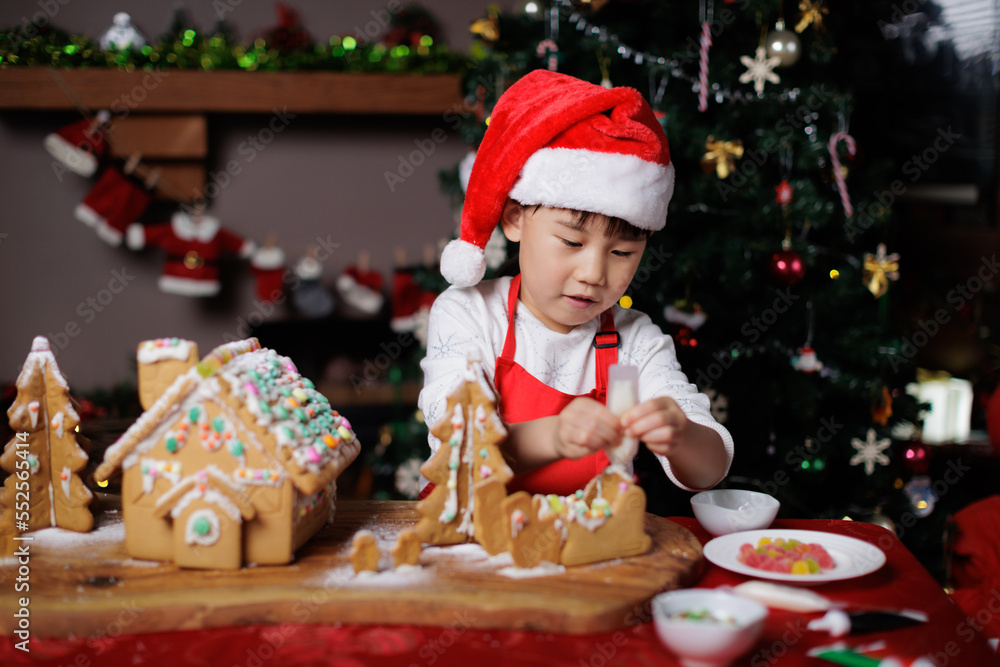 young girl wearing Santa hat was decorating gingerbread house for celebrating Christmas at home young girl wearing Santa hat was decorating gingerbread house for celebrating Christmas at home