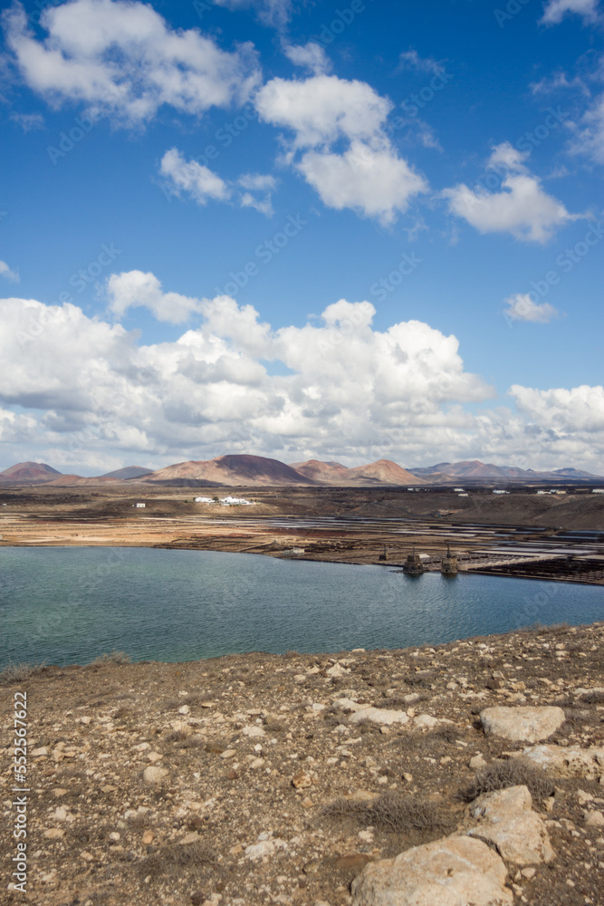 Deserted landscape of some old salt pans. salt pans constructions. Calm ocean. mountains in the background. Clear sky with big white fluffy clouds. Sand and rocks. Lanzarote, Canary Islands, Spain.