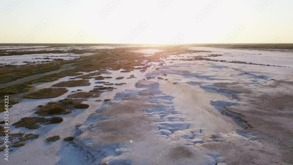 moving aerial view of a salt field,  with little vegetation and a sunset sky