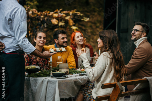 Photography Group of elegantly dressed friends having a small boho dinner/wedding outdoors in a garden, drinking wine, and talking to each other with a great mood and smiles