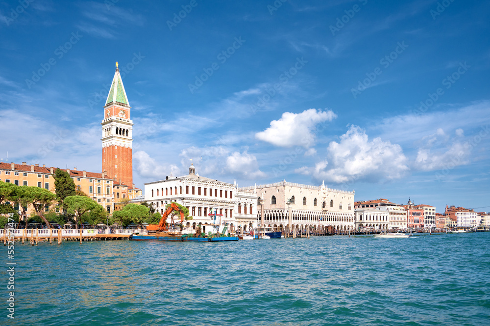 Doge's palace and Campanile on Piazza di San Marco, Venice, Italy with sea water on foreground. Calm sunny day in Summer, blue sky with clouds.