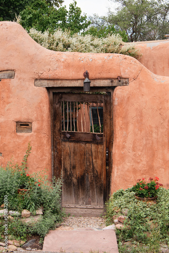 Weathered wood door and old adobe wall with flower pots with red flowers in Santa Fe, New Mexico