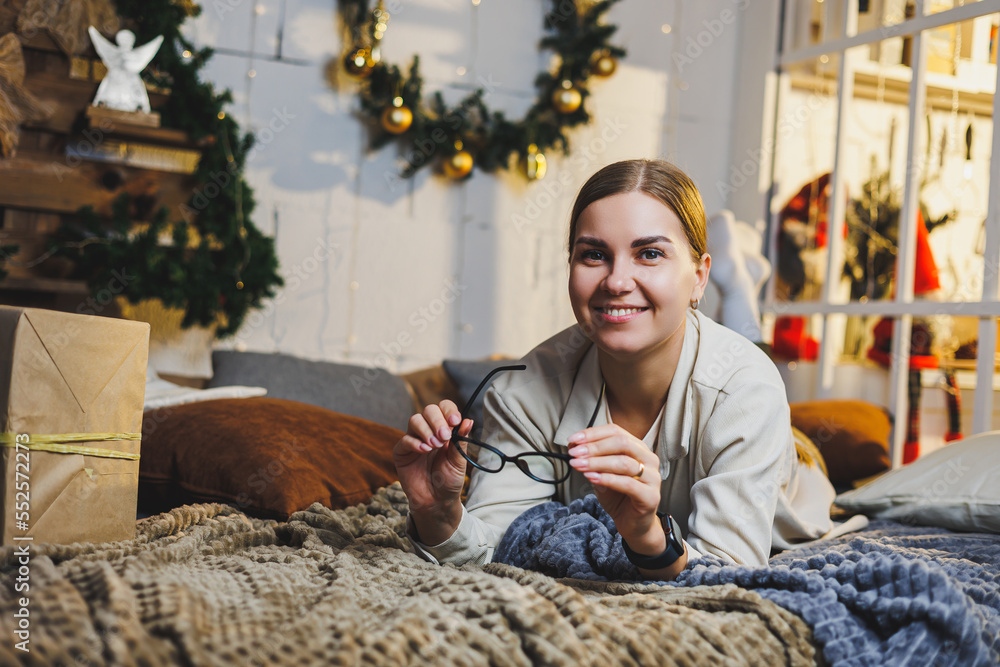 Obraz premium Portrait of a happy smiling woman against the background of New Year's decorations. The woman is happy with the Christmas holidays. New Year's atmosphere at home