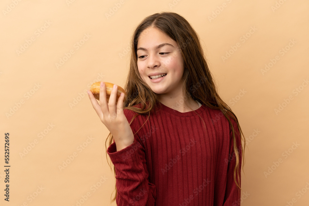 Little caucasian girl isolated on beige background holding donuts with happy expression Little caucasian girl isolated on beige background holding donuts with happy expression
