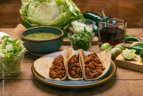Marinated beef tacos, bowl with salsa verde and vegetables on a wooden table. Tacos de adobada.