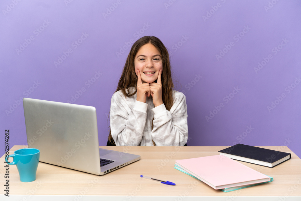 Little student girl in a workplace with a laptop isolated on purple background smiling with a happy and pleasant expression Little student girl in a workplace with a laptop isolated on purple background smiling with a happy and pleasant expression
