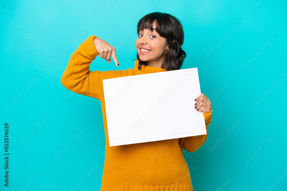 Young latin woman isolated on blue background holding an empty placard with happy expression and pointing it Young latin woman isolated on blue background holding an empty placard with happy expression and pointing it