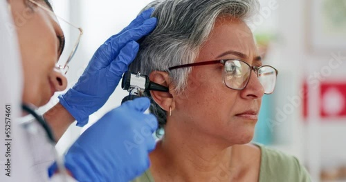 Doctor, elderly patient and ear exam, test or medical checkup for hearing aid or diagnosis at the hospital. Hands of audiologist with otoscope helping senior woman for audiology healthcare at clinic photo