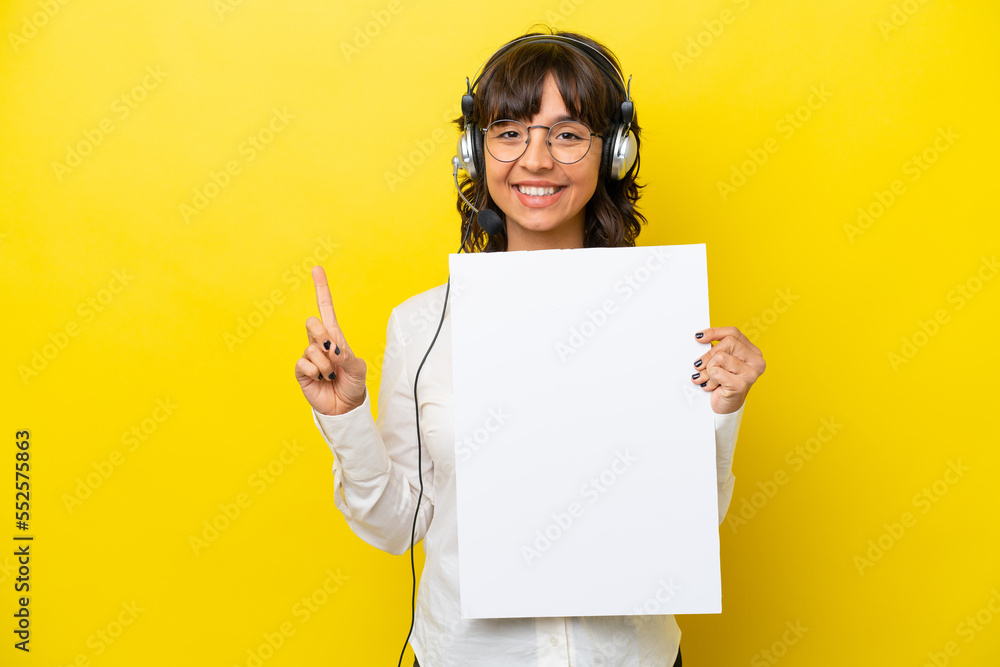 Telemarketer latin woman working with a headset isolated on yellow background holding an empty placard and pointing up Telemarketer latin woman working with a headset isolated on yellow background holding an empty placard and pointing up