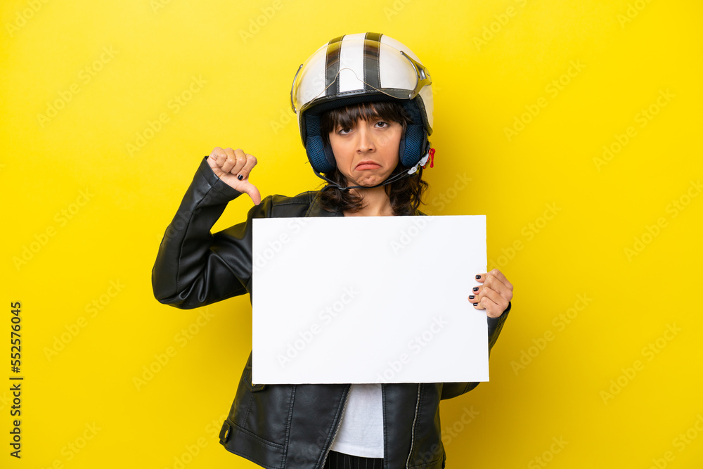 Young latin woman with a motorcycle helmet isolated on yellow background holding an empty placard and doing bad signal Young latin woman with a motorcycle helmet isolated on yellow background holding an empty placard and doing bad signal