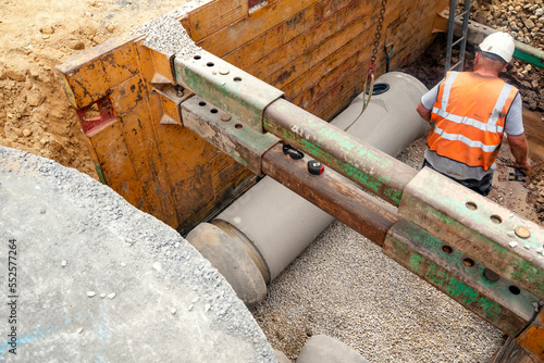Builder installing big diameter concrete drainage pipe protected by trench support system during deep drainage works photo