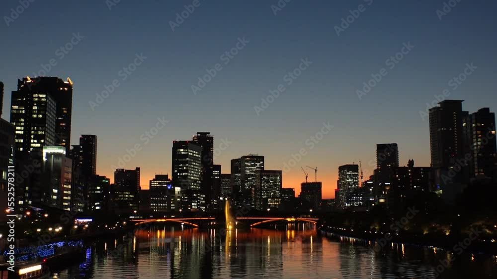 OSAKA, JAPAN - SEP 2022 : Office buildings at Kitahama area and river in sunset. Large business district in Osaka. Time lapse shot, dusk to night. Japanese business, company and urban city concept. OSAKA, JAPAN - SEP 2022 : Office buildings at Kitahama area and river in sunset. Large business district in Osaka. Time lapse shot, dusk to night. Japanese business, company and urban city concept.