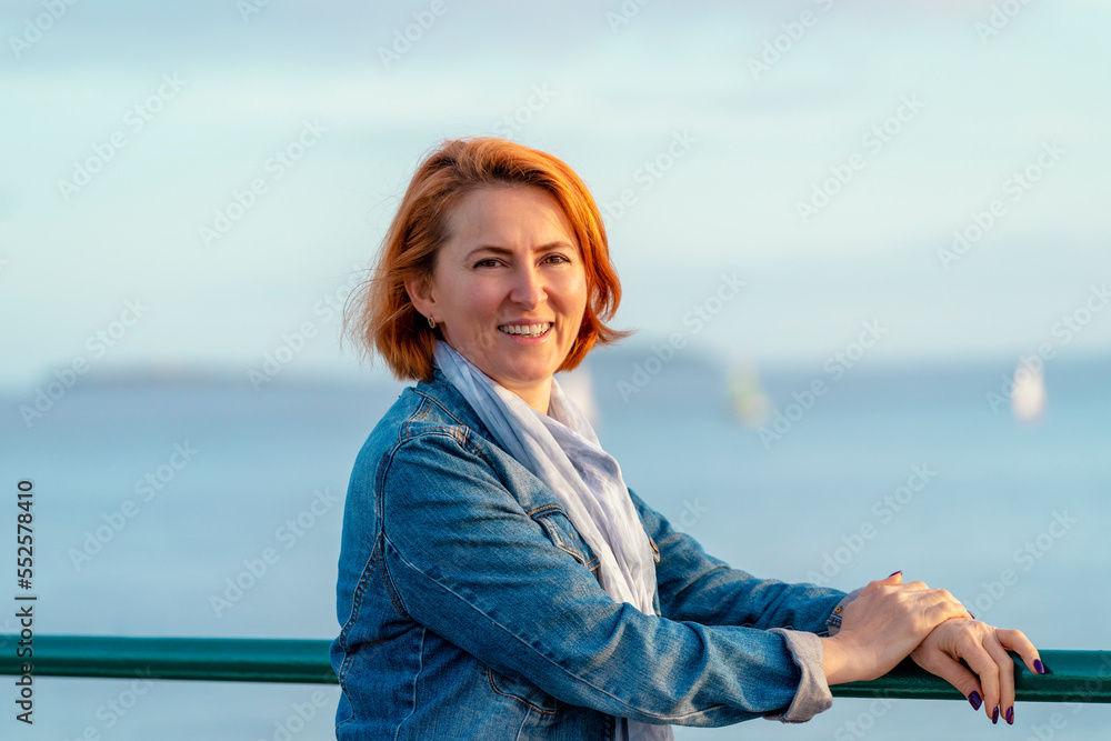 red womanl in blue dress and jeans jacket  resting on the seashore at sunset