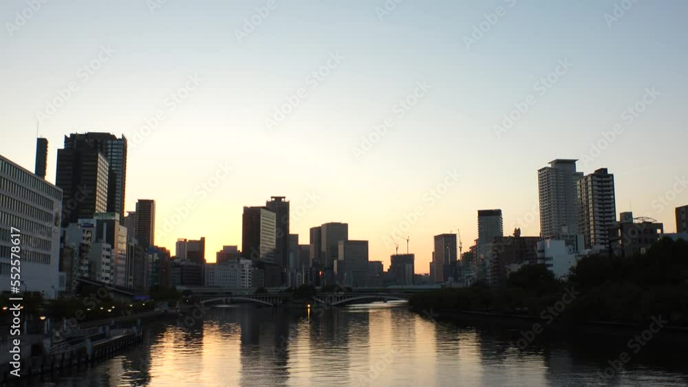 OSAKA, JAPAN - SEP 2022 : Office buildings at Kitahama area and river in sunset. Large business district in Osaka. Time lapse shot, dusk to night. Japanese business, company and urban city concept. OSAKA, JAPAN - SEP 2022 : Office buildings at Kitahama area and river in sunset. Large business district in Osaka. Time lapse shot, dusk to night. Japanese business, company and urban city concept.