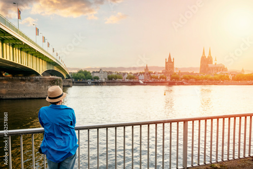 woman in hat and blue shirt on embankment of Rhine on background of Cologne Cathedral and Hohenzollern Bridge in Koel, Germany. Tourism and travel by Germany concept photo