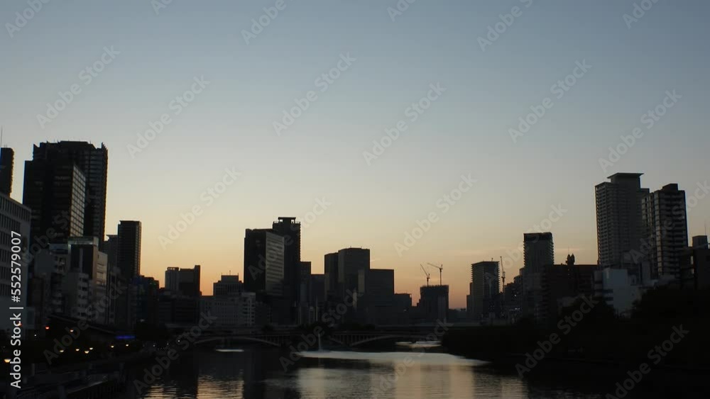 OSAKA, JAPAN - SEP 2022 : Office buildings at Kitahama area and river in sunset. Large business district in Osaka. Time lapse shot, dusk to night. Japanese business, company and urban city concept.