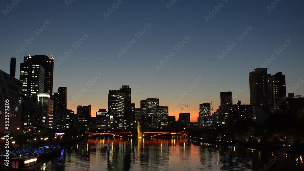 OSAKA, JAPAN - SEP 2022 : Office buildings at Kitahama area and river in sunset. Large business district in Osaka. Time lapse shot, dusk to night. Japanese business, company and urban city concept. OSAKA, JAPAN - SEP 2022 : Office buildings at Kitahama area and river in sunset. Large business district in Osaka. Time lapse shot, dusk to night. Japanese business, company and urban city concept.