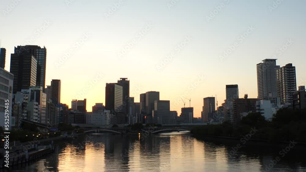 OSAKA, JAPAN - SEP 2022 : Office buildings at Kitahama area and river in sunset. Large business district in Osaka. Time lapse shot, dusk to night. Japanese business, company and urban city concept. OSAKA, JAPAN - SEP 2022 : Office buildings at Kitahama area and river in sunset. Large business district in Osaka. Time lapse shot, dusk to night. Japanese business, company and urban city concept.