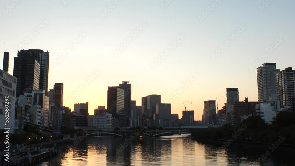 OSAKA, JAPAN - SEP 2022 : Office buildings at Kitahama area and river in sunset. Large business district in Osaka. Time lapse shot, dusk to night. Japanese business, company and urban city concept. OSAKA, JAPAN - SEP 2022 : Office buildings at Kitahama area and river in sunset. Large business district in Osaka. Time lapse shot, dusk to night. Japanese business, company and urban city concept.
