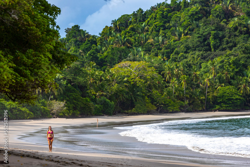 Fotografie A beautiful girl in a pink bikini walks on a tropical beach with palm trees in m
