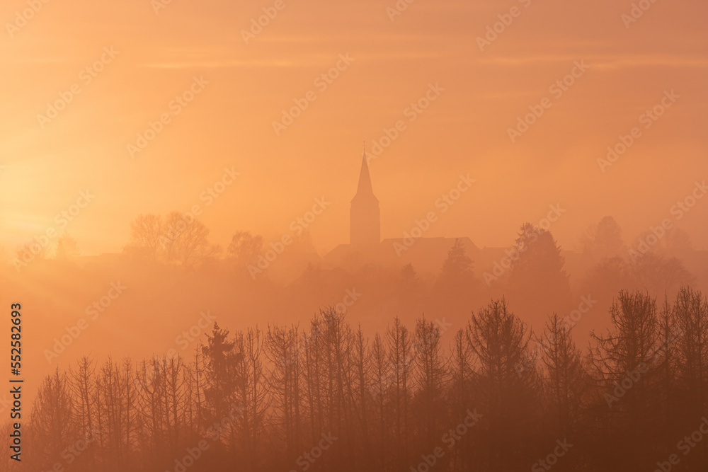 Fototapeta premium Aerial view of a church with trees in the foreground in the warm tones of sunset in Germany, dramatic sky