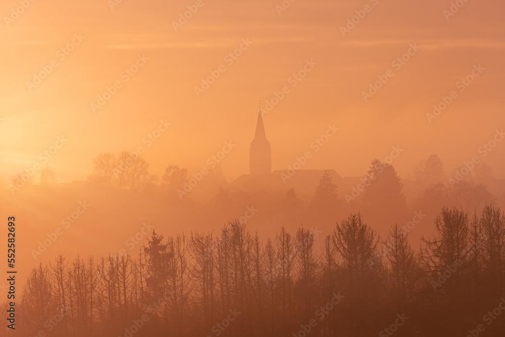 Aerial view of a church with trees in the foreground in the warm tones of sunset in Germany, dramatic sky