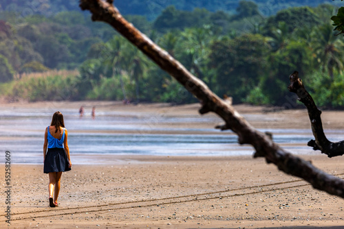 A beautiful girl in a short skirt walks on a paradisiacal tropical beach in marino ballena national park, Costa Rica; Costa Rica beach panorama with palm trees and mountains in the background