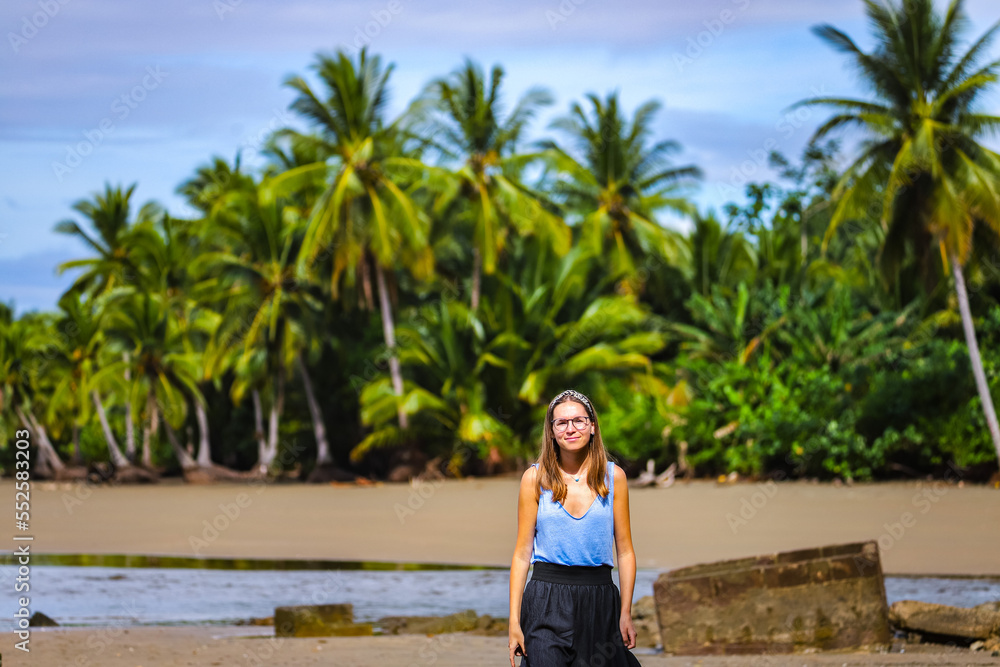 a lone beautiful girl in a skirt walks along a tropical beach with palm trees in marino ballena national park in costa rica; relaxing on a paradise beach in costa rica