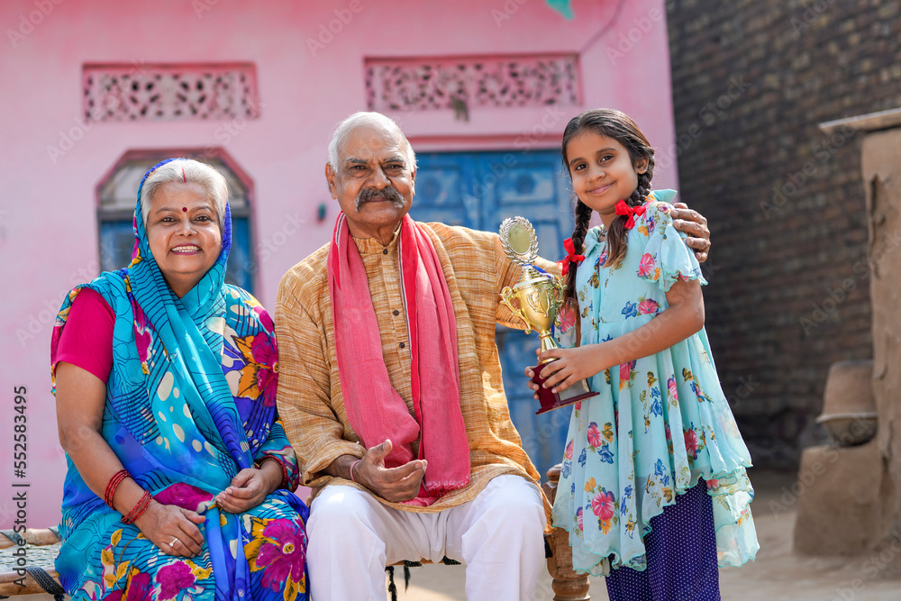 Fototapeta premium Indian little girl holding winning trophy with grandparents