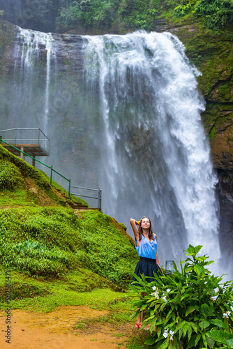 A beautiful girl in a short skirt stands under eco chontales waterfall in Costa Rica; a massive waterfall in the rainforest in Costa Rica photo