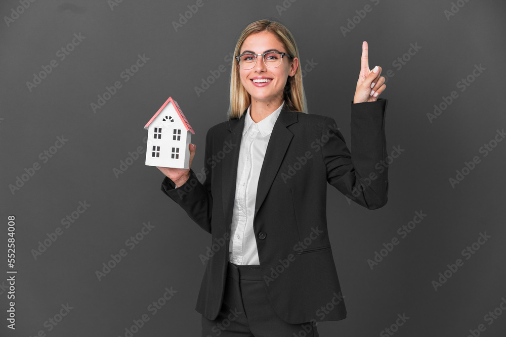 Blonde Uruguayan girl holding a house toy isolated on black background pointing up a great idea Blonde Uruguayan girl holding a house toy isolated on black background pointing up a great idea