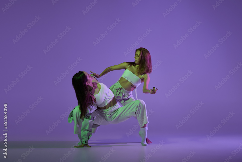 Experimental dance. Two young girl in motion, action isolated over purple background. Emotions, love, style, youth, music and fashion