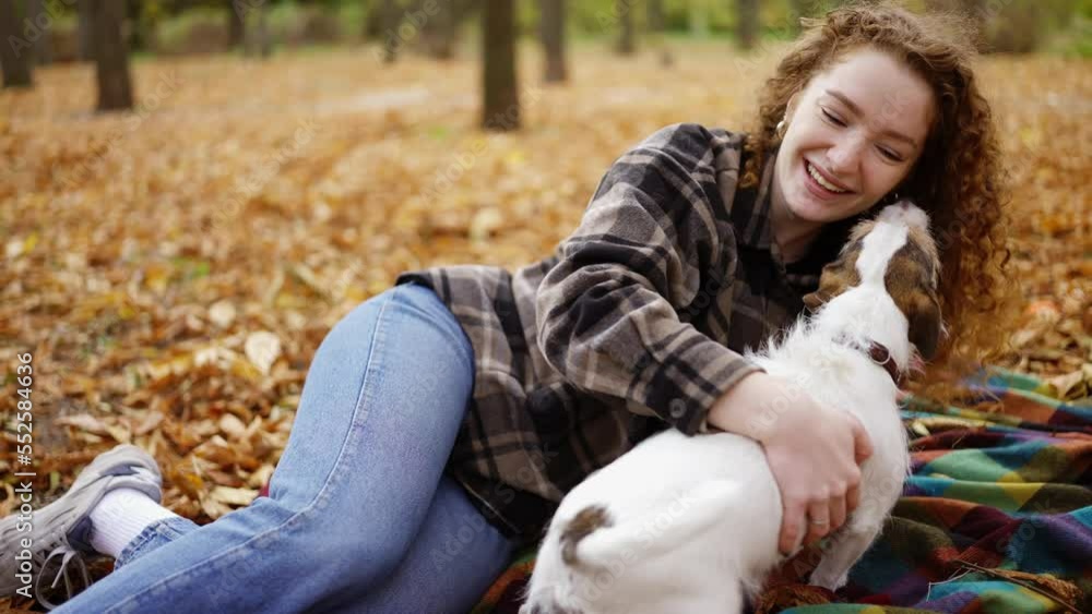 Curly woman laying on a plaid with her jack russell terrier puppy in autumn park Curly woman laying on a plaid with her jack russell terrier puppy in autumn park